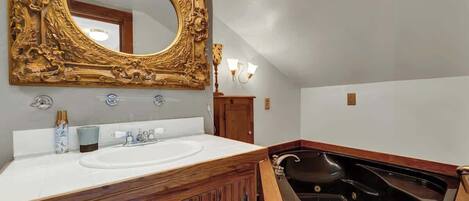 Un baño con tocador de madera, un espejo grande y decorativo, una bañera y un lavamanos blanco.
