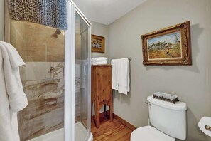 A bathroom with a shower, toilet, and a framed painting on the wall. - Gillespie House-2 Suites-walk to Main St! (Fredericksburg)