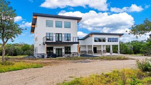 A modern two-story house with a large driveway, a covered outdoor area, and a landscaped garden. - Hill Country Escape W/views Plus, Hot-tub and Pet Friendly! (Kerrville)