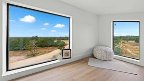 A room with large windows offering a view of a landscape with trees and a dirt path. - Hill Country Escape W/views Plus, Hot-tub and Pet Friendly! (Kerrville)