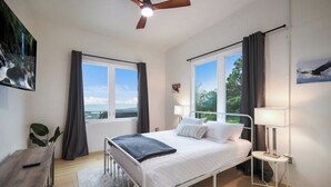 A bedroom with a bed, bedside tables, a ceiling fan, and large windows.