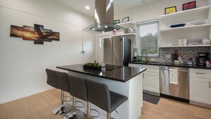 A modern kitchen with a central island, bar stools, stainless steel appliances, and a herringbone-patterned backsplash.