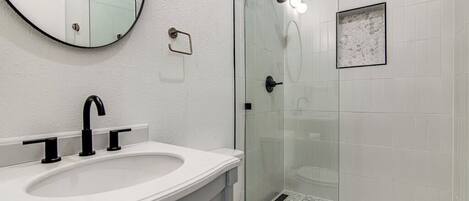 Une salle de bain avec un lavabo blanc, un robinet noir et un miroir rond.