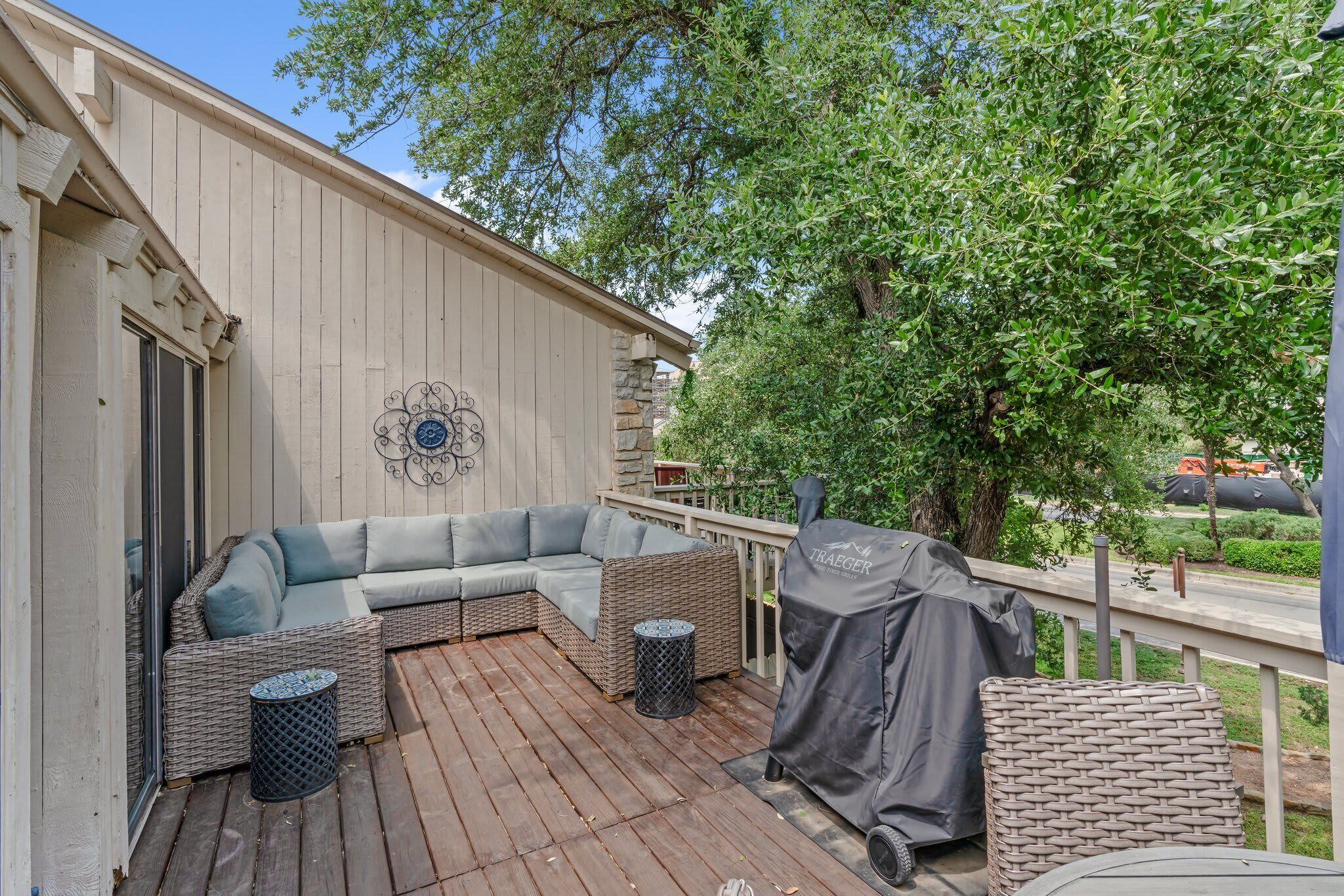 A covered outdoor deck with wicker furniture, a grill, and a stone wall.