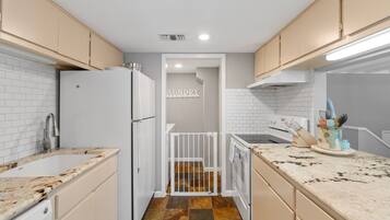 Una cocina con armarios blancos, un refrigerador blanco, salpicadero de azulejos y un letrero que dice 'AUNDRY'.