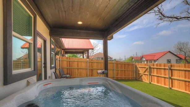 Un jacuzzi bajo una pérgola de madera con vistas a un patio trasero y casas vecinas.