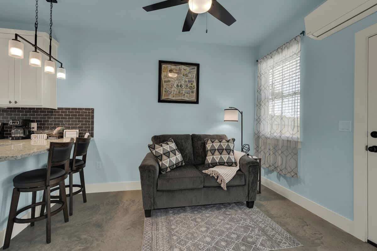 A compact living space with a kitchenette, a sofa with patterned cushions, a ceiling fan, and a framed map on the wall.