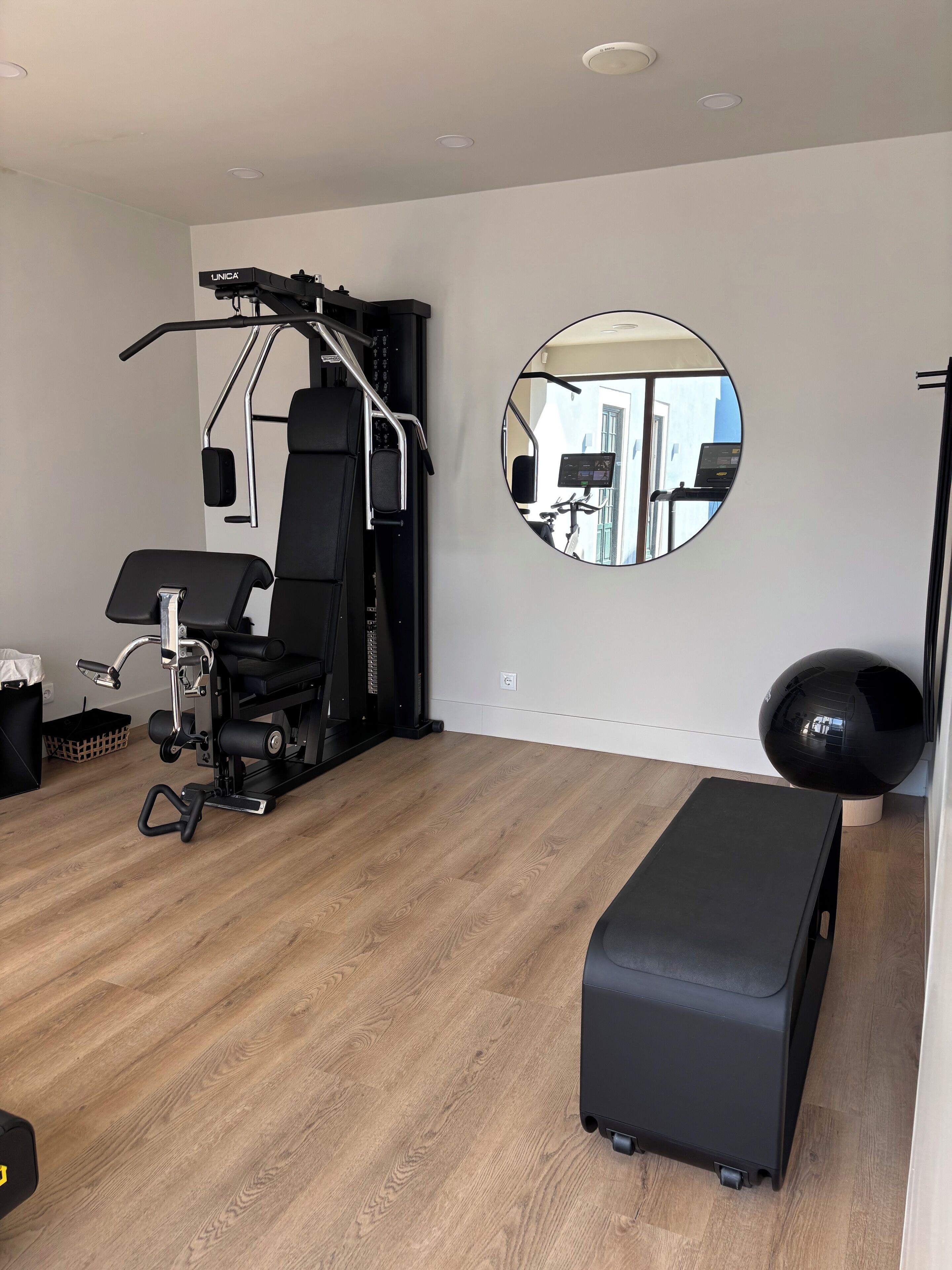 Ein Fitnessraum mit Trainingsgeräten, einer Bank, einem Spiegel und einem Fenster.