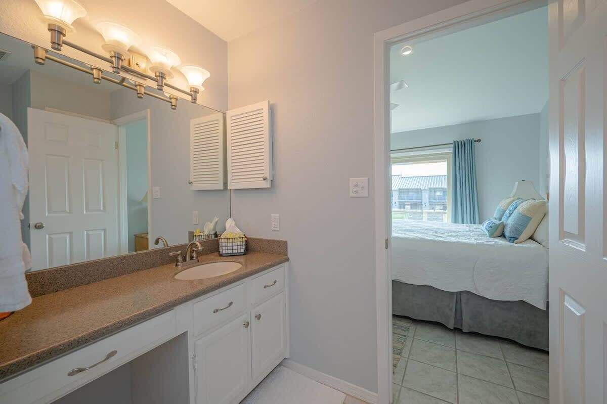 A bathroom with a sink, mirror, and vanity. There is a bed visible through an open door.