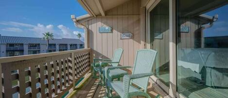 A balcony with wicker chairs, a ceiling fan, and a view of a building with palm trees.