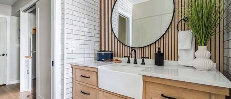 Un baño moderno con lavamanos blanco, tocador de madera y un espejo grande.