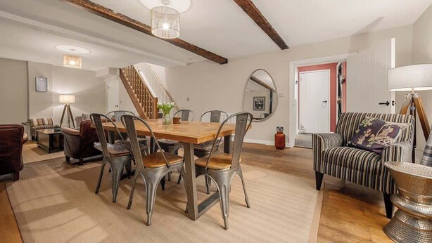 Ein Essbereich mit Holztisch und Metallstühlen, einer Treppe und einem gestreiften Ohrensessel.