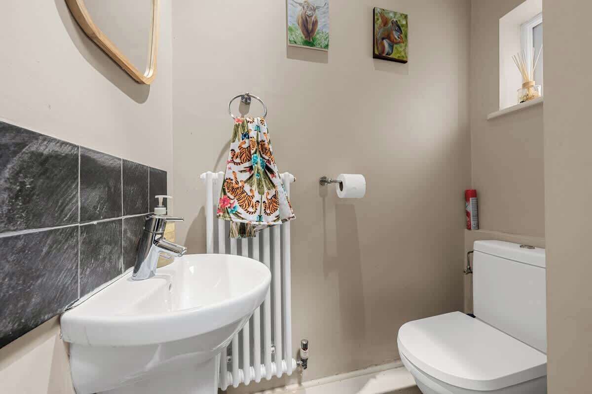 Een badkamer met een wit wastafelmeubel, toilet en radiator. Twee foto's hangen in lijsten aan de muur.