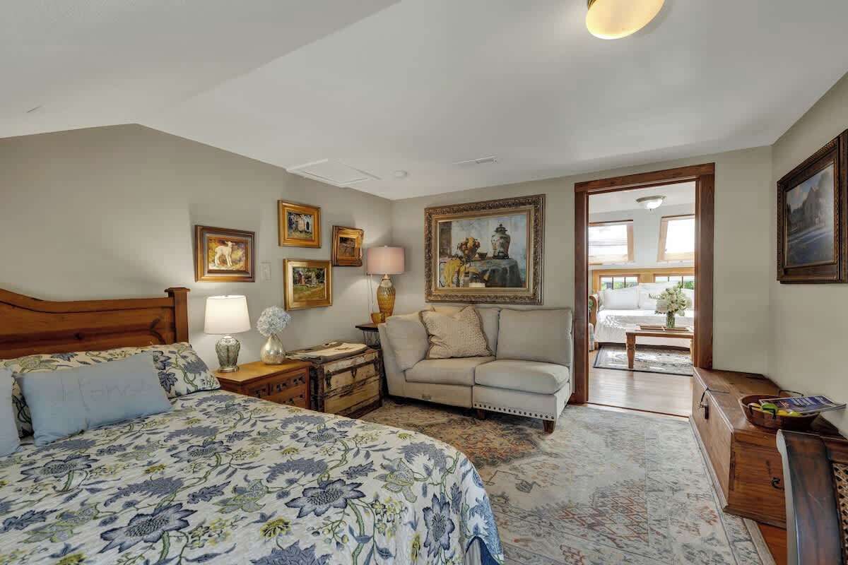 A bedroom with a bed, a nightstand, a lamp, a dresser, a sofa, and a painting on the wall.