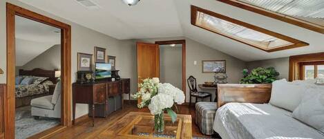 A spacious loft bedroom with a large bed, a wooden coffee table, a desk, and a view of the sky through skylights.