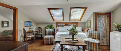 A loft-style bedroom with a bed, two skylights, a dining area, and a living room with a sofa and chairs.