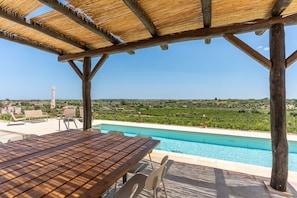 Uma pérgola de madeira com piscina e área de estar ao ar livre, com vista para um vinhedo.