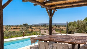 Un espace aménagé au bord de la piscine, avec une table et des chaises en bois, offrant une vue sur un paysage pittoresque.