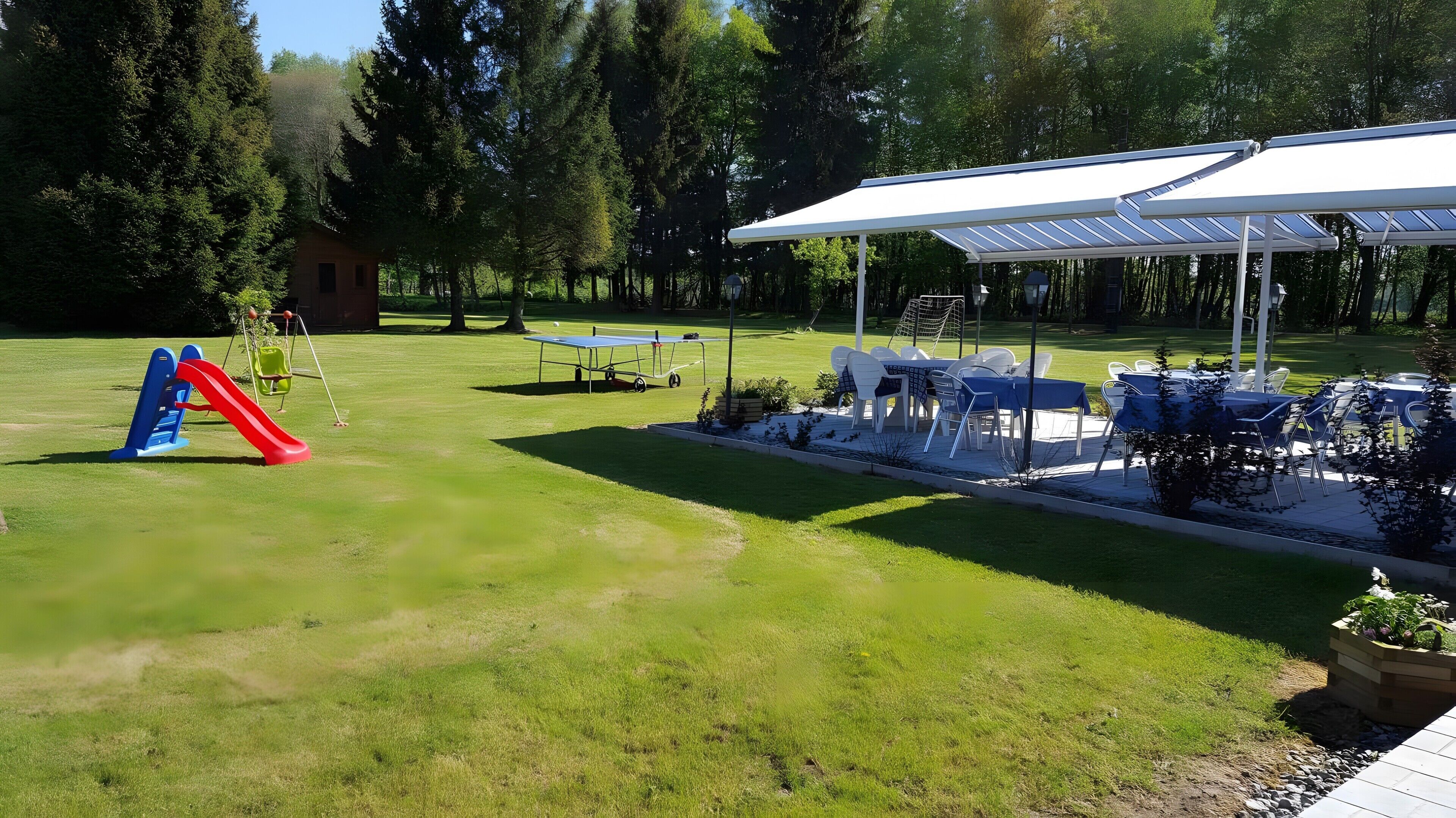 Un espacio exterior bien cuidado con un parque infantil, mesas para picnic y una zona de estar cubierta con paneles solares.