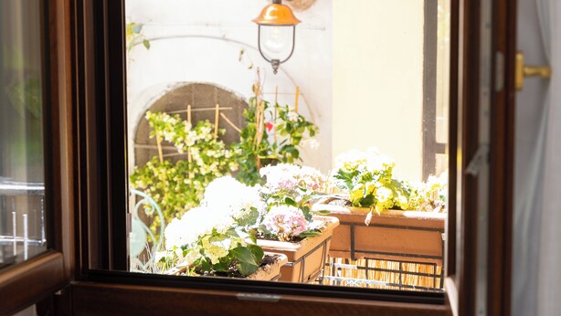 Une fenêtre donnant sur un balcon agrémenté de plantes en pot et muni d’un luminaire fixé au mur.