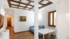 Une pièce avec un plancher en bois, un canapé bleu, une table à manger en verre et une fenêtre avec des rideaux.