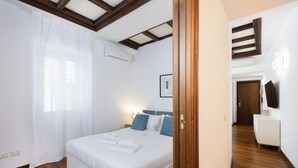 Une chambre avec un plafond en bois, un lit avec une literie blanche, une table de chevet et un téléviseur fixé au mur.