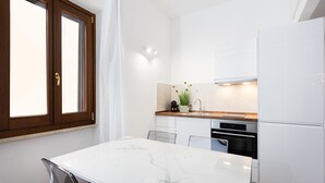 Une cuisine moderne avec des meubles blancs, un plan de travail en marbre et un four encastré.