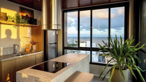 A modern kitchen with a large island, a stainless steel range hood, and a view of the city through large windows. - Unforgettable stay between Farol and Barra Mall (Salvador)