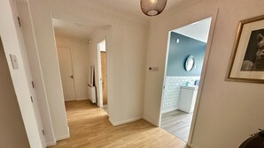 Un pasillo con piso de madera que conduce a un baño con una pared azul de acento y un espejo redondo.