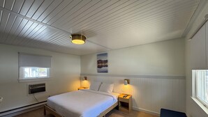 Un dormitorio con cama de madera, lámparas de noche, una ventana y un cuadro colgado en la pared.