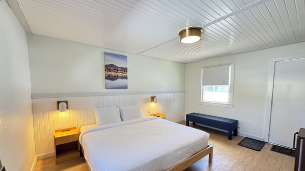 Un dormitorio moderno con una cama de madera, dos lámparas de noche, un banco, una ventana y una lámpara de techo.