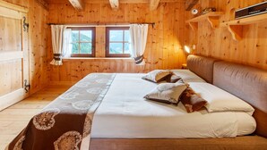 Ein Holzhütten-Zimmer mit Bett, Vorhängen, einem Fenster und einem Regal mit Gegenständen.