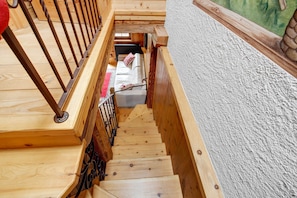Un escalier en bois mène à une pièce dont le mur est blanc et où se trouve un tapis rouge.