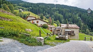 Ein ländliches Dorf mit traditionellen Steinhäusern, einem Kopfsteinpflasterweg und einer Bergkulisse.