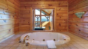 Ein Holzblock-Interieur mit einer großen Badewanne, einem Fenster mit Blick auf eine Terrasse und einer Deckenleuchte.