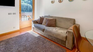 A living room with a sofa, a glass table, a brown rug, and a door leading to a balcony.