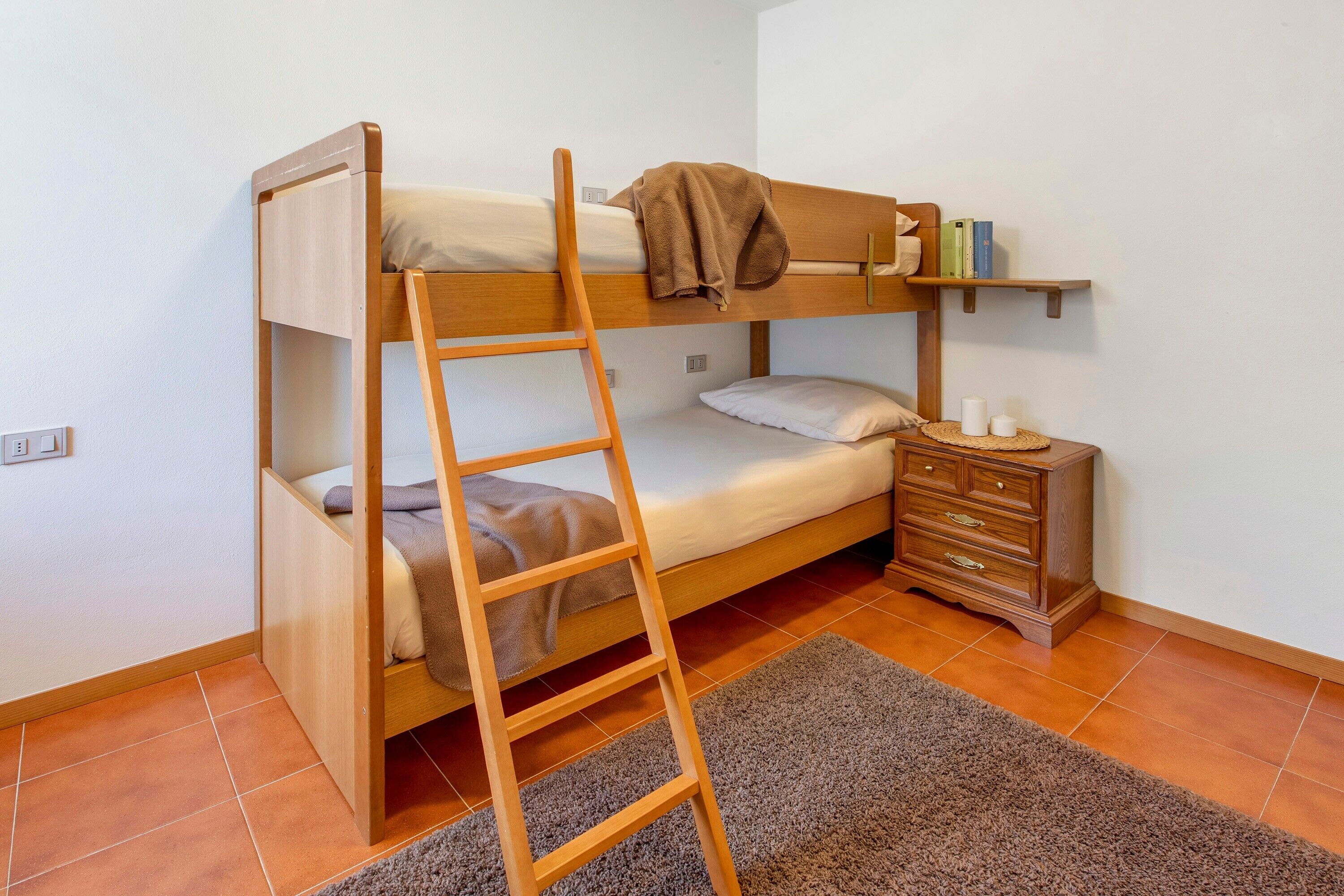 A bunk bed with a ladder, a bedside table with books, and a small drawer unit.