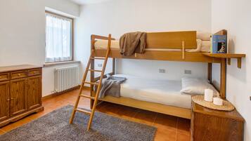 A bunk bed room with a ladder, a bedside table with candles, a book, and a window with curtains.