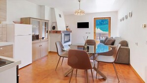 A modern kitchen with a dining area, a TV mounted on the wall, and a large window with a view.