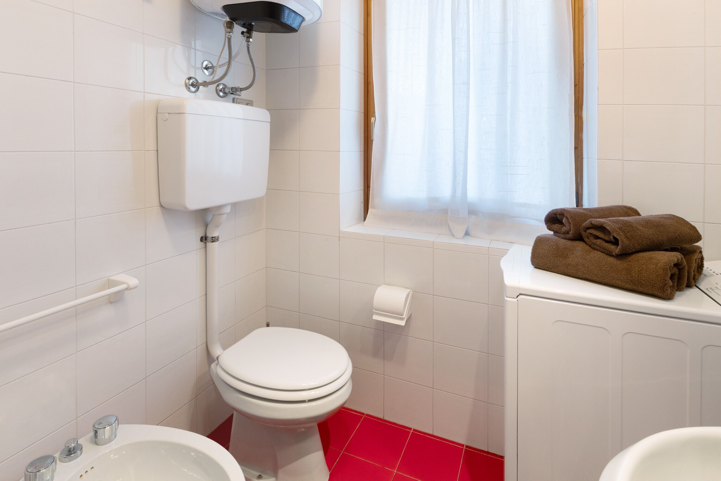 Un baño con inodoro, bidé y ventana con cortinas.
