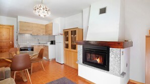 A modern kitchen with a fireplace, wooden cabinets, and a dining area with chairs and a table.
