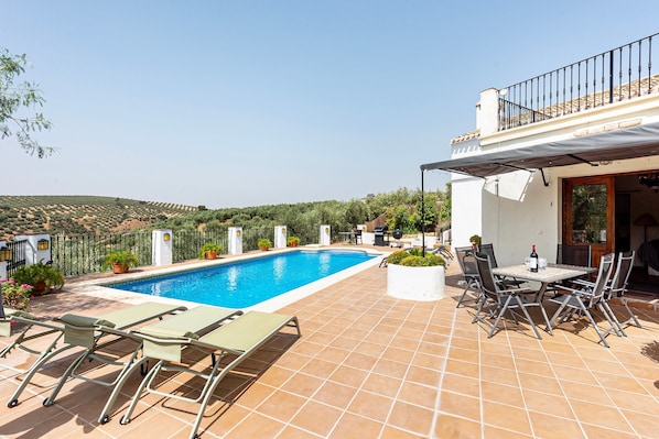 A swimming pool with lounge chairs and a table, surrounded by a tiled patio.