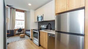 A modern kitchen with stainless steel appliances, wooden cabinets, and a small dining area with a table and chairs. - Studio 613 at The Frank (Birmingham)