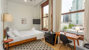 A hotel room with a bed, desk, chair, TV, and large windows offering a city view. - Studio 613 at The Frank (Birmingham)