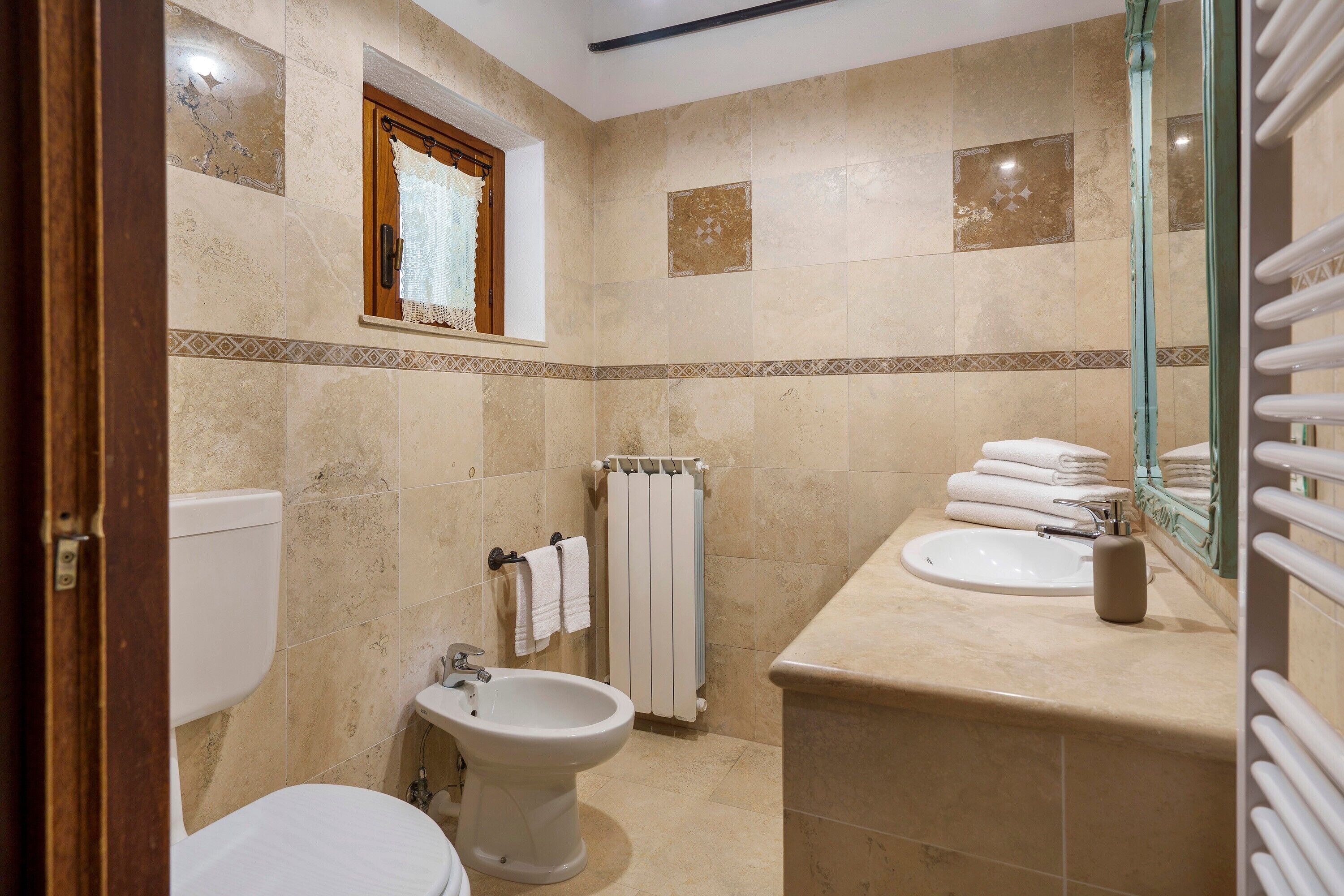 A bathroom with a toilet, bidet, sink, and a towel rack with folded towels.
