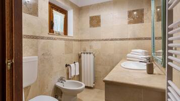 A bathroom with a toilet, bidet, sink, and a towel rack with folded towels.