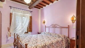 A bedroom with a wooden bed, a window with a lace curtain, and a nightstand with a lamp.