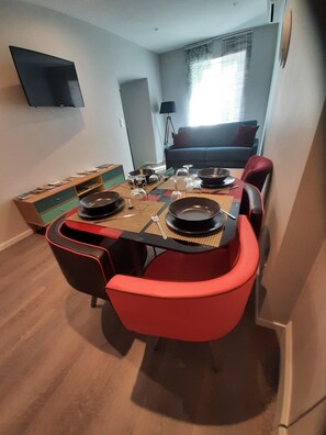 Un coin repas avec une table dressée pour quatre personnes, un canapé en arrière-plan et un téléviseur fixé au mur.