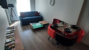 A living room with a sofa, a coffee table, a TV, and a clock on the wall. - Apartment 102 - Cosy T2 60 m² (Bourg-Saint-Andéol)