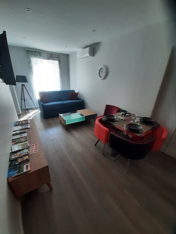 Un salon avec un canapé, une table basse, un téléviseur et une horloge au mur.